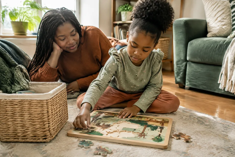 Child aged six peacefully using a large wooden puzzle from a quiet-time basket in a sunny living room corner.