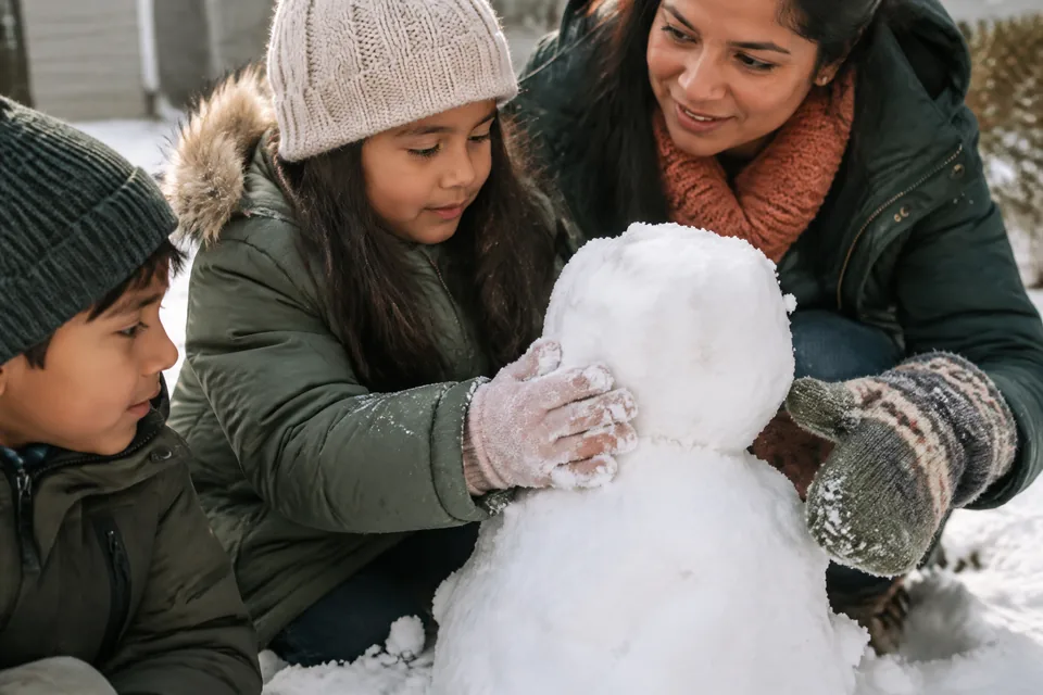 Gloved school-age hands shaping a snow figure with a parent's mitten nearby.